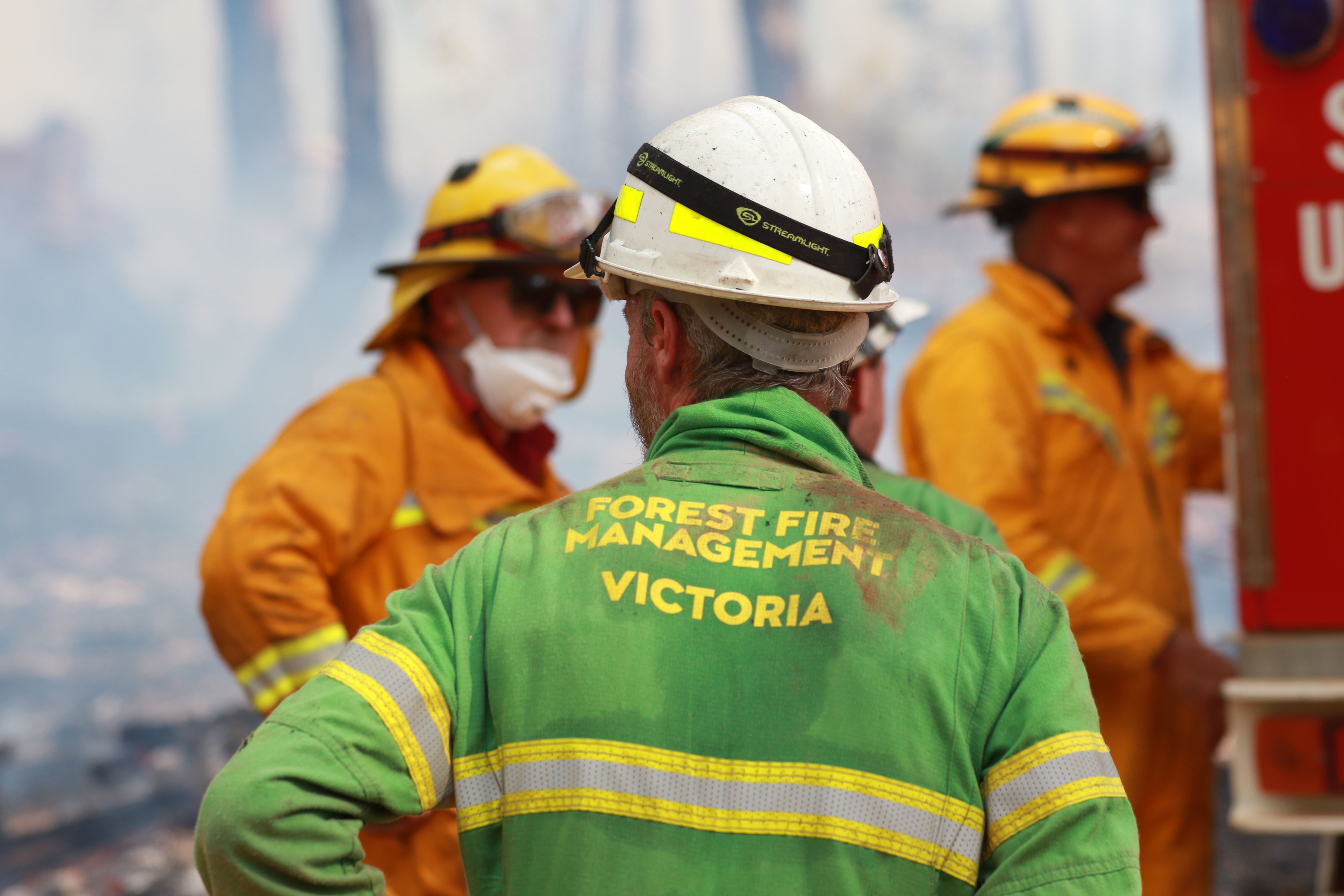 The back of a man wearing a Forest Fire Management Victoria emergency clothing, in a smoky haze.