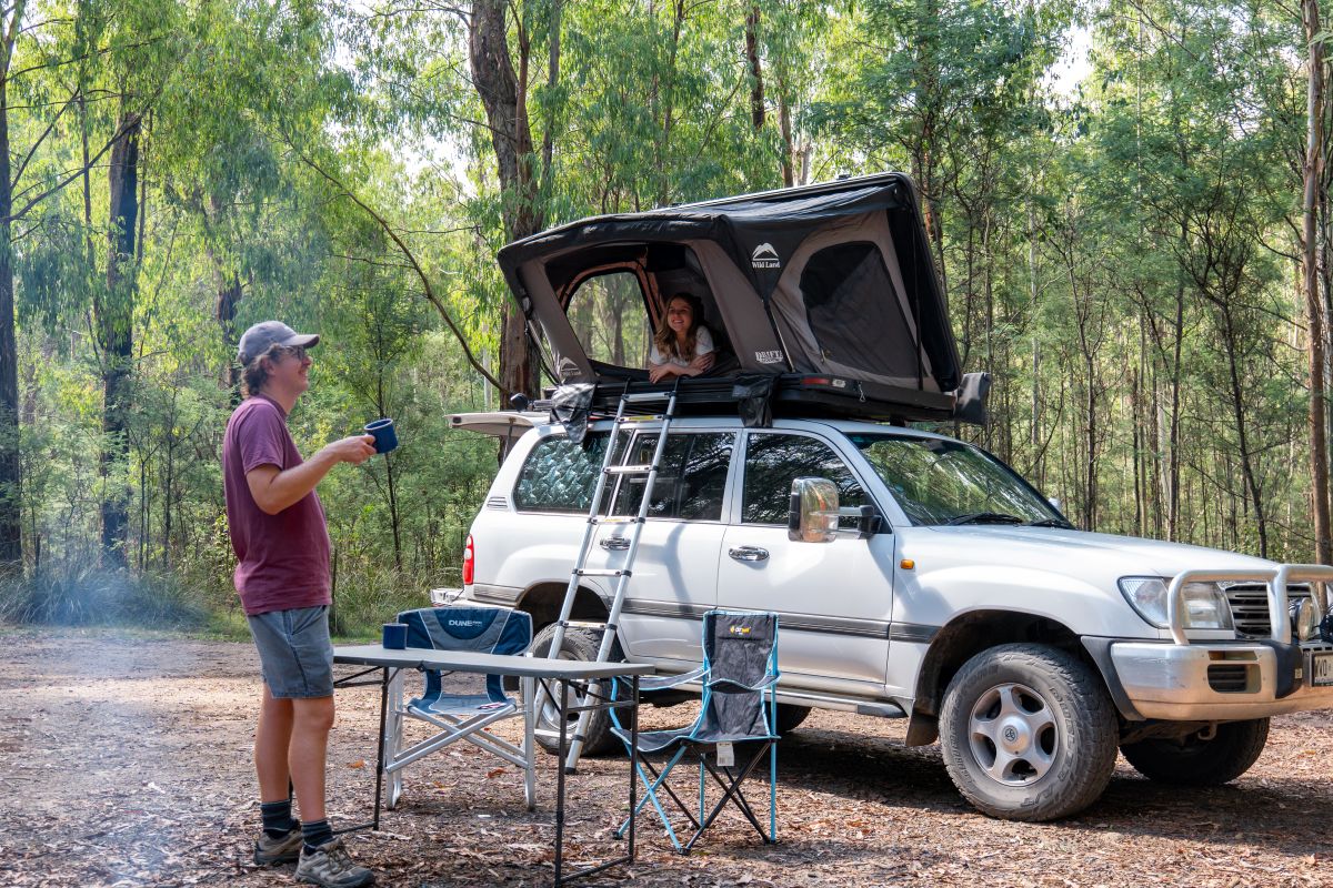 A man with his family holding a cup of coffee, his daughter in the tent over his truck