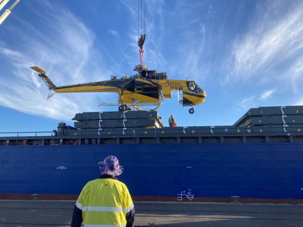Man in fluro shirt and patterned hat watches on as aircrane 'Marty' is lifted by a crane